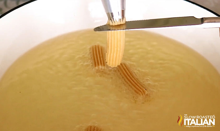 slicing churro dough into pot of oil as it comes out of piping bag