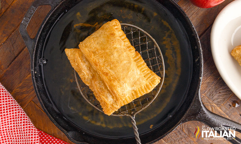 lifting fried apple pie out of oil with strainer