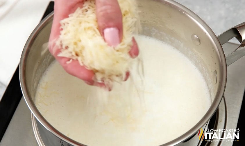 adding shredded cheese to pot of alfredo