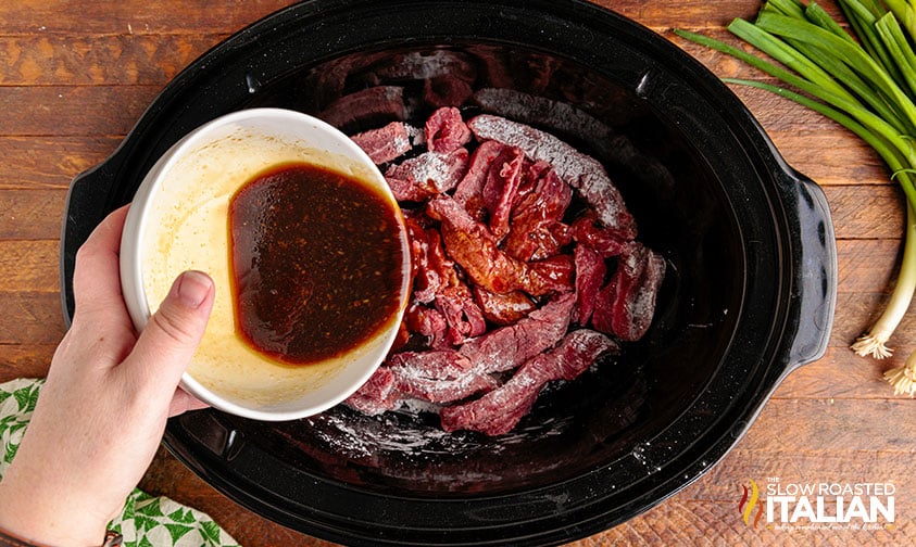pouring sauce over beef slices in crockpot