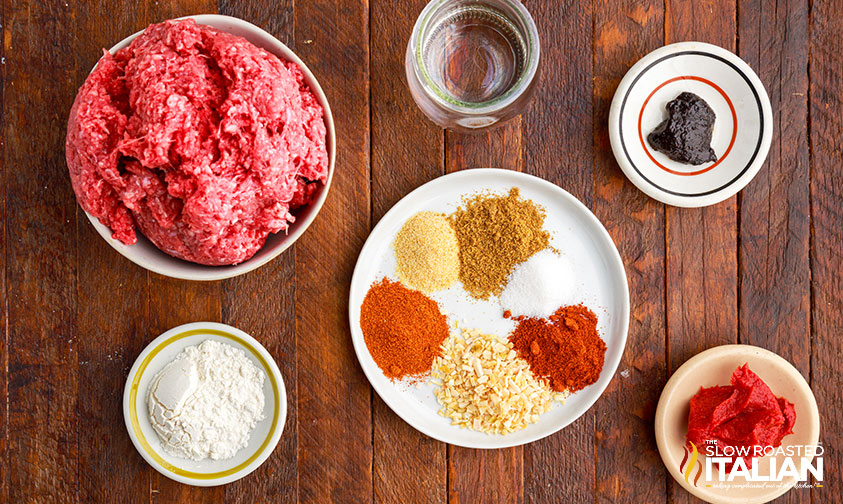 recipe ingredients in bowls including a bowl of ground beef, flour, sauces and plate of seasoning