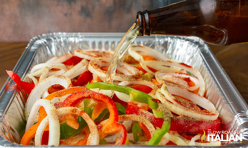 pouring beer over brats and veggies in foil pan
