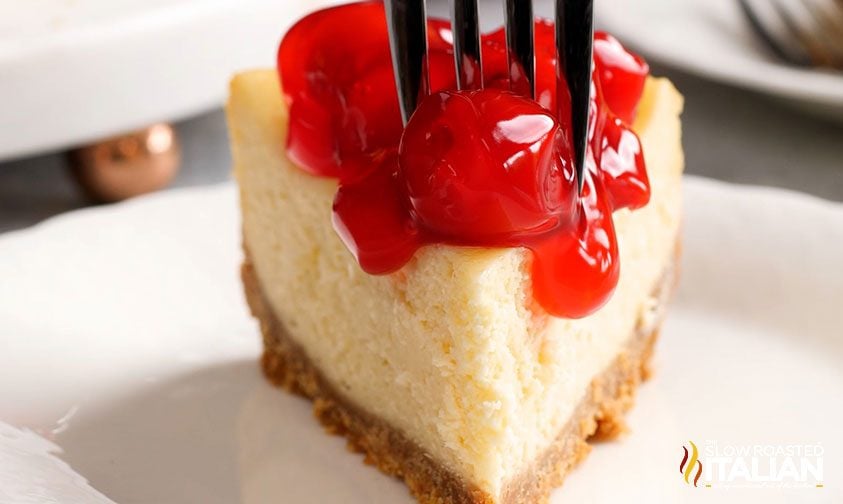 fork in slice of cheesecake with cherry topping