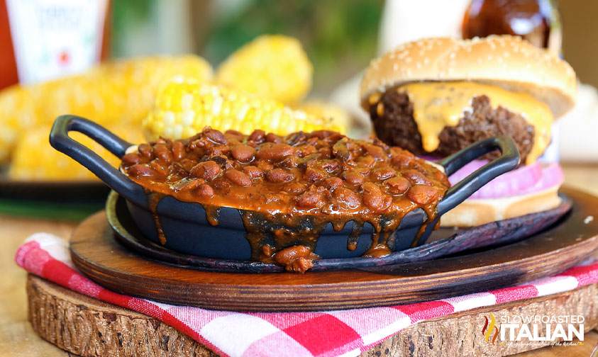 small pan of baked beans on plate with burger and corn