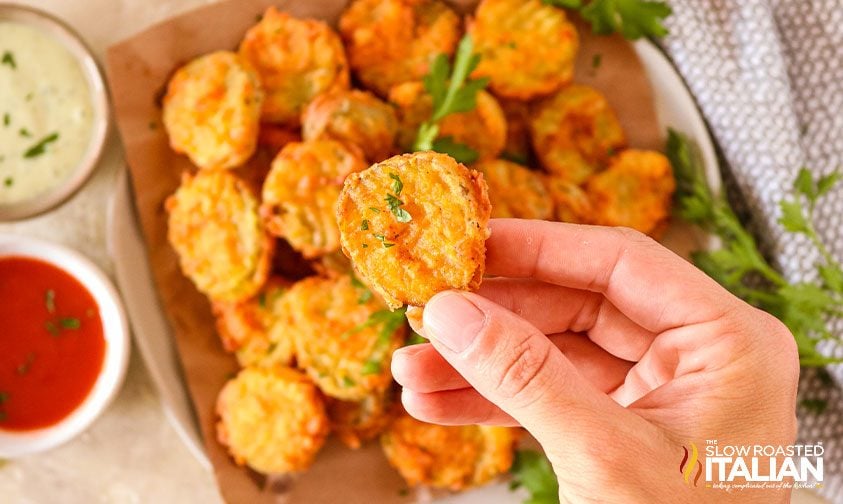 holding a fried pickle chip above a full tray