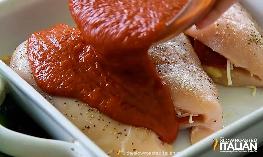 pouring marinara over italian stuffed chicken breasts