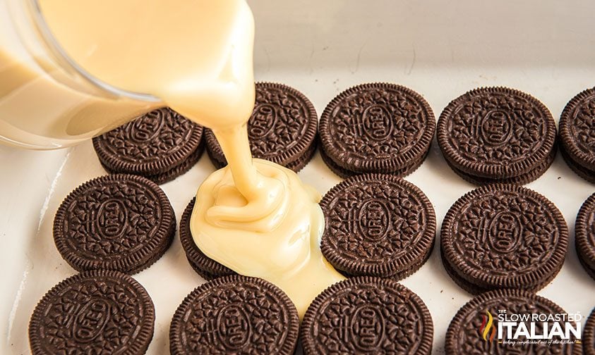 pouring sweetened condensed milk over oreos in baking dish