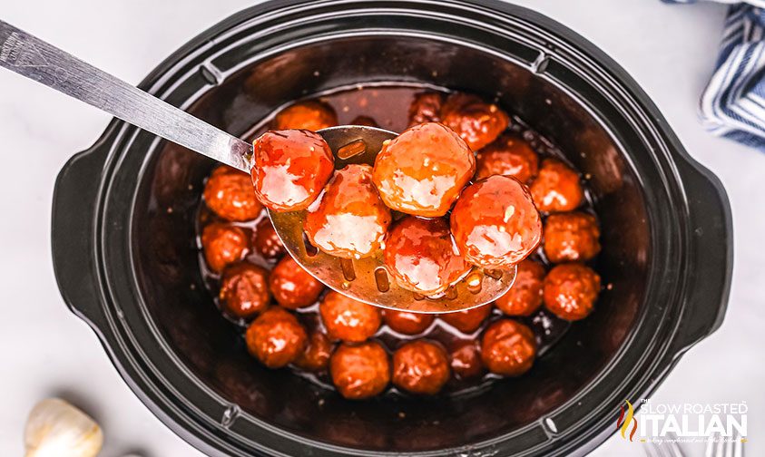scooping meatballs with sauce out of crockpot