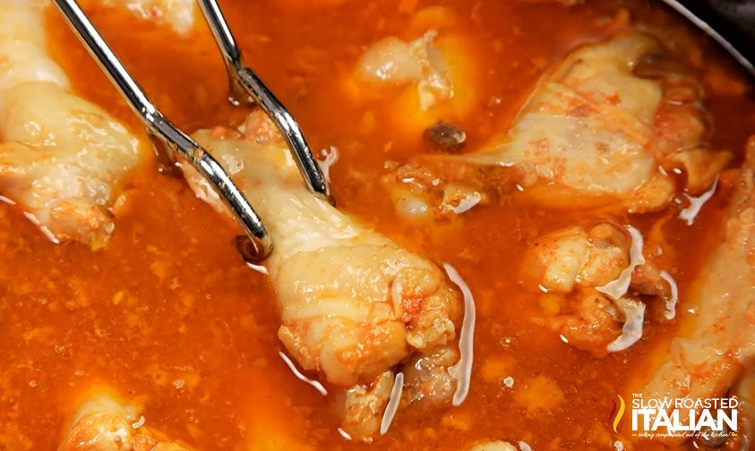 tongs grabbing chicken wing in sauce