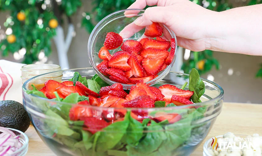 adding strawberries to bowl of spinach