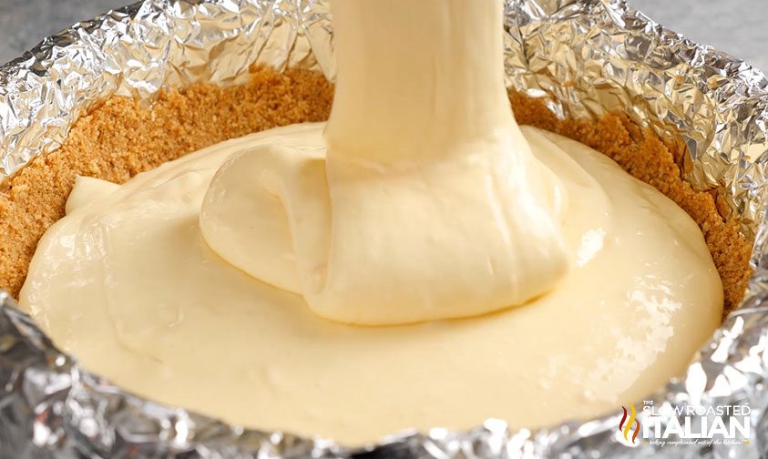 close up: pouring cheesecake filling over crust in foil lined pan