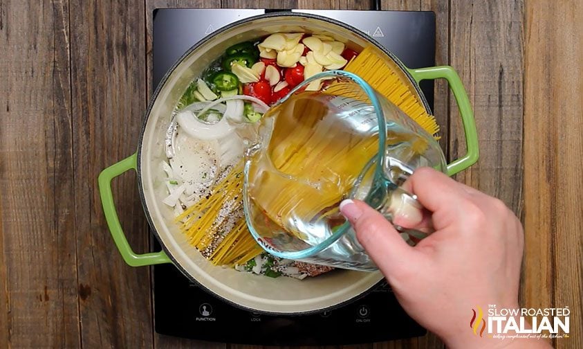 pouring water over Mexican pasta ingredients in pot