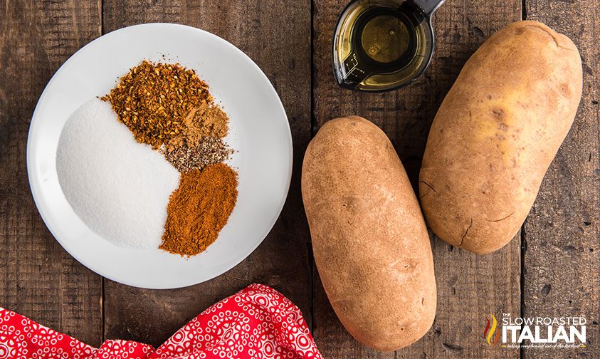 plate of spices next to two Russet potatoes and measuring cup with oil