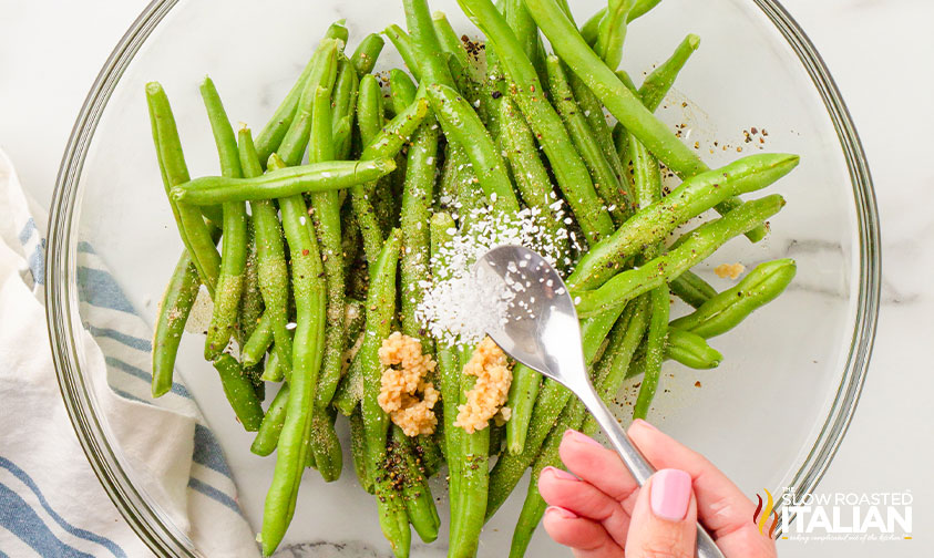 sprinkling seasonings over bowl of fresh green beans