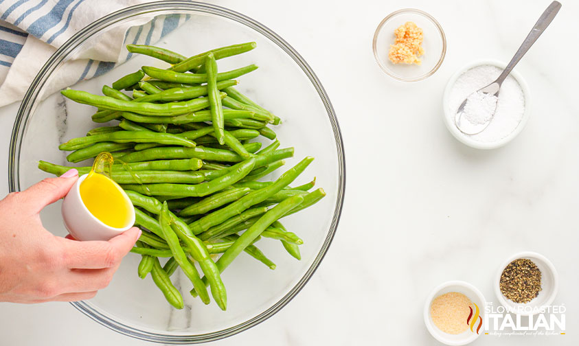 drizzling oil over fresh green beans with spices nearby