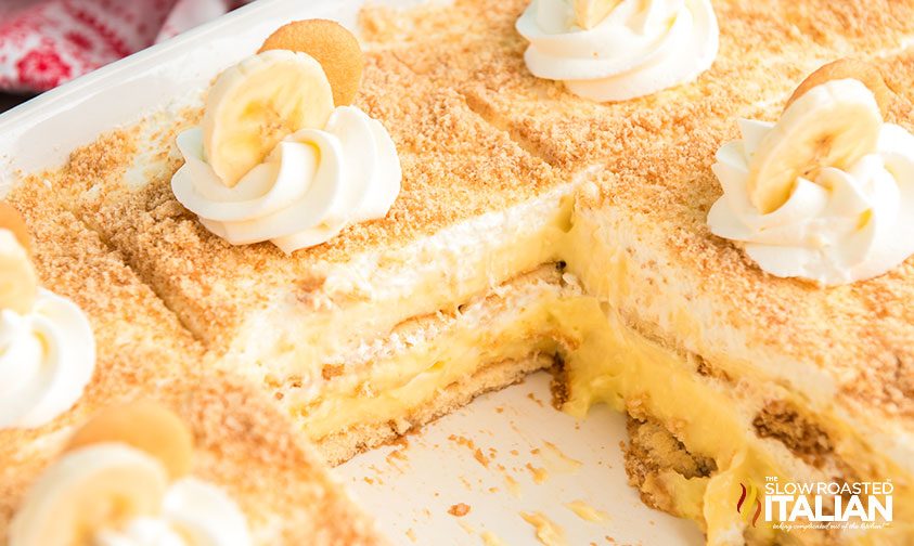 sliced banana pudding cake in a baking dish with a piece removed