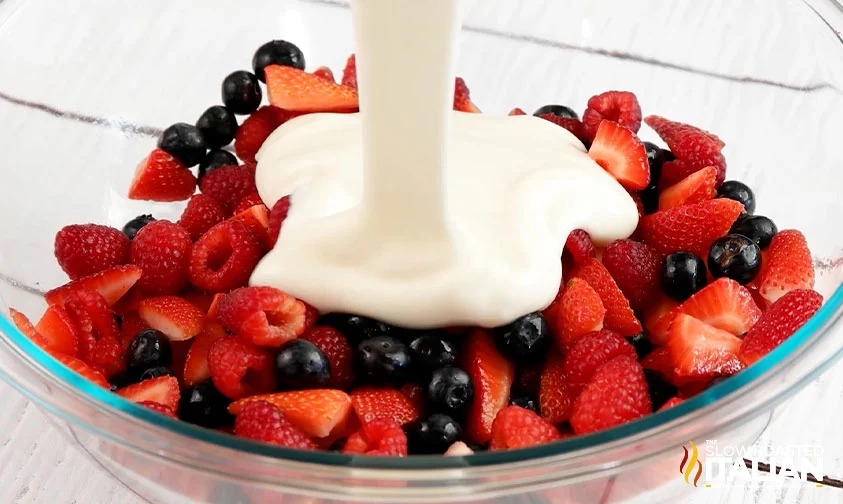 pouring cheesecake filling over berries in a bowl