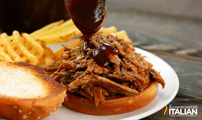 drizzling bbq sauce over pulled pork on bun