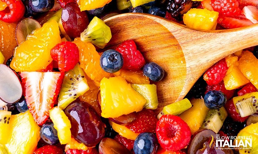 close up: stirring fruit salad dressing into fresh fruit and berries
