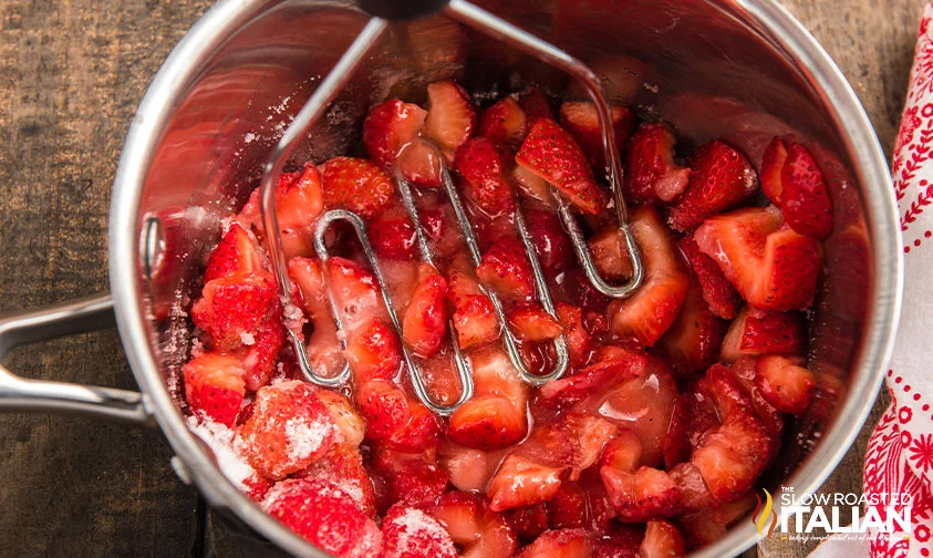 mashing strawberries with sugar in saucepan