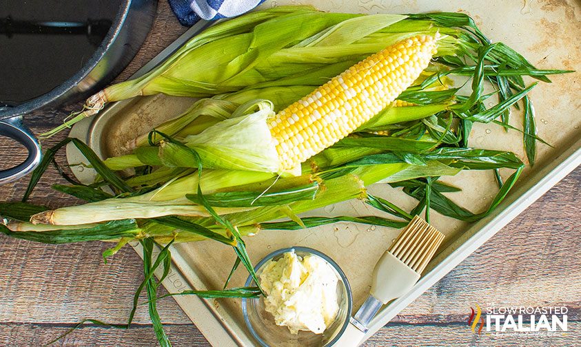 husk peeled back from corn to apply seasoned butter mixture