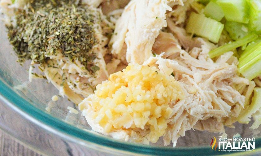 close up: shredded chicken, celery, minced garlic, and spices in bowl