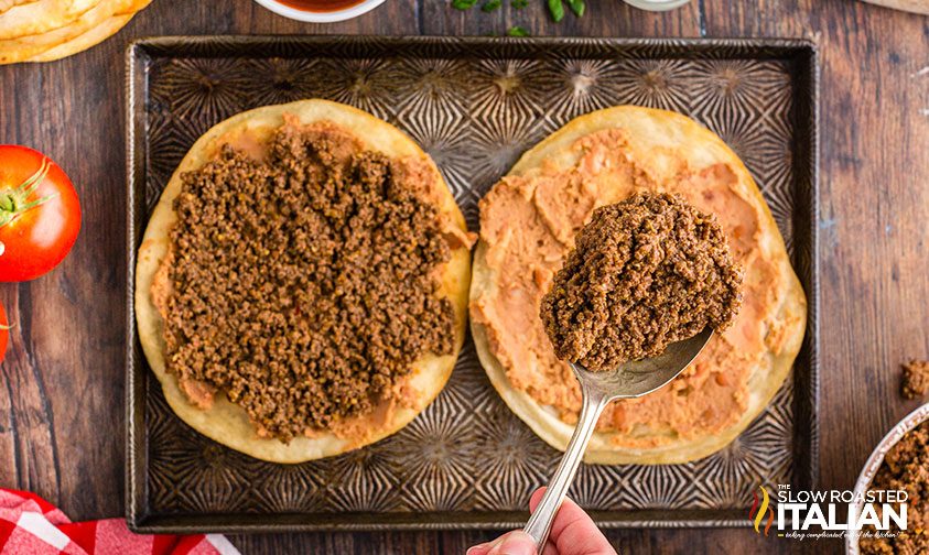 spooning ground beef over fried tortillas with refried beans