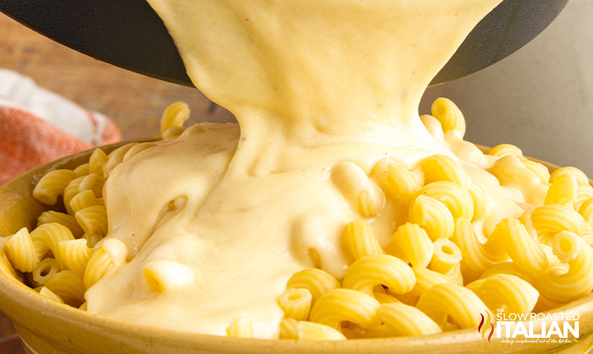 pouring spicy cheese sauce over cooked pasta