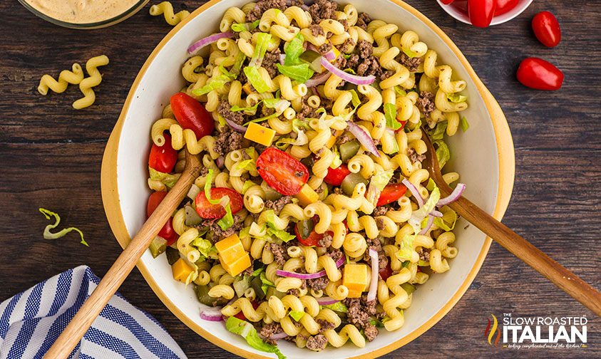 bowl of tossed Big Mac salad ingredients with two wooden spoons