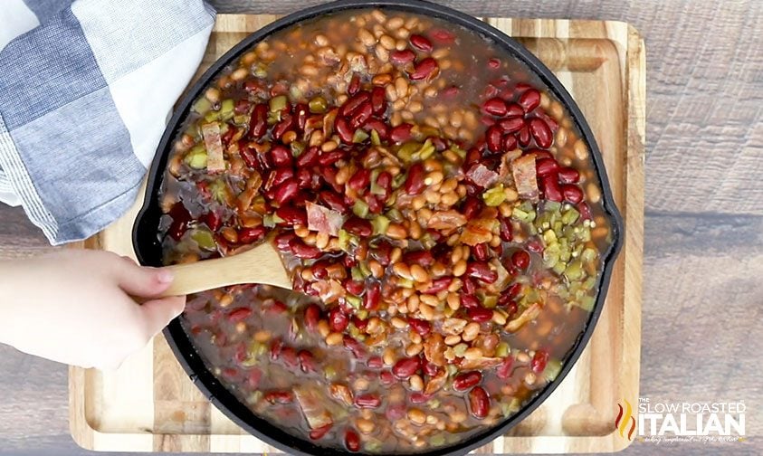 stirring smoked beans ingredients in cast iron pan