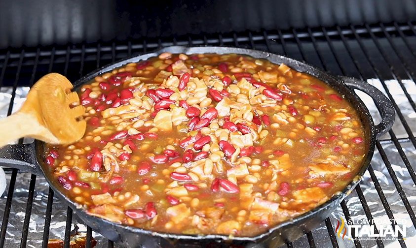 stirring smoker baked beans in cast iron pan