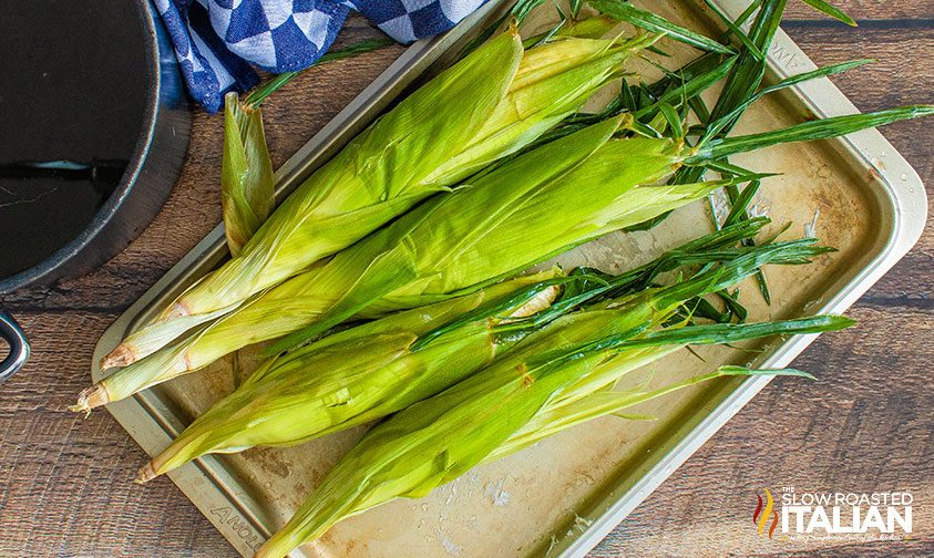 corn in husks on baking sheet