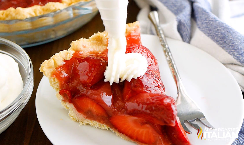 piping whipped cream onto slice of strawberry pie