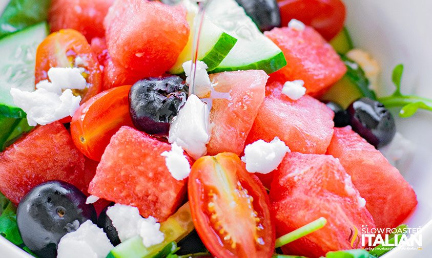 drizzling oil dressing over watermelon blueberry feta salad