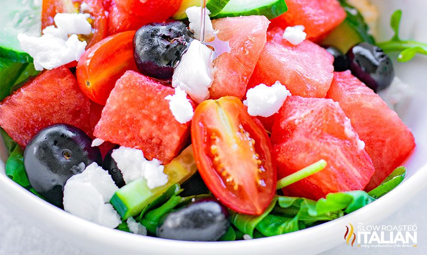 close up: sliced watermelon, grape tomatoes, greens, blueberries, and feta in a bowl