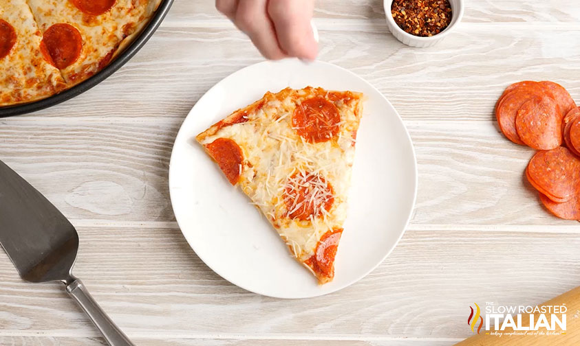 sprinkling parmesan over a slice of pepperoni pizza