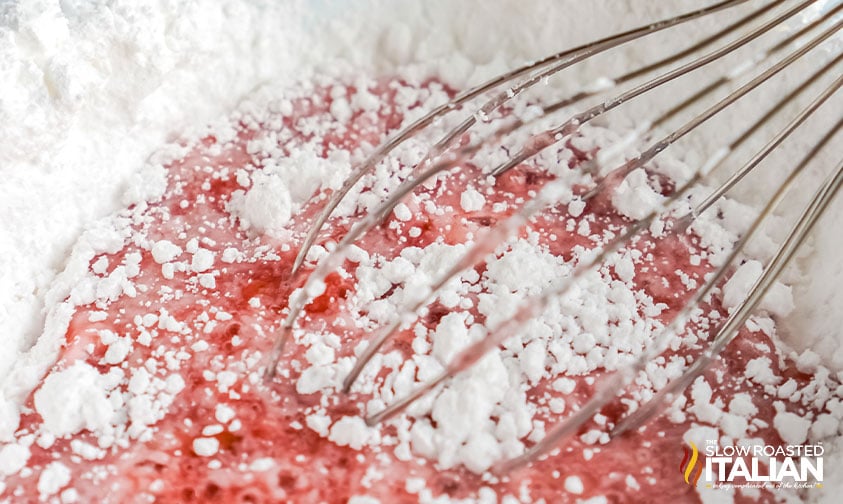 whisking powdered sugar into strawberry simple syrup