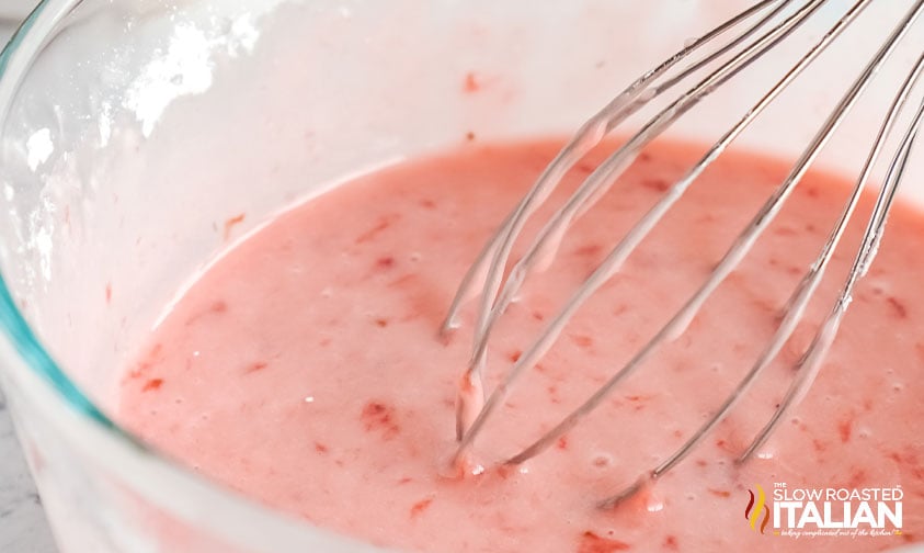 metal whisk in bowl of strawberry glaze