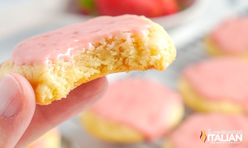 holding a cookie with strawberry icing that has a bite taken out of it