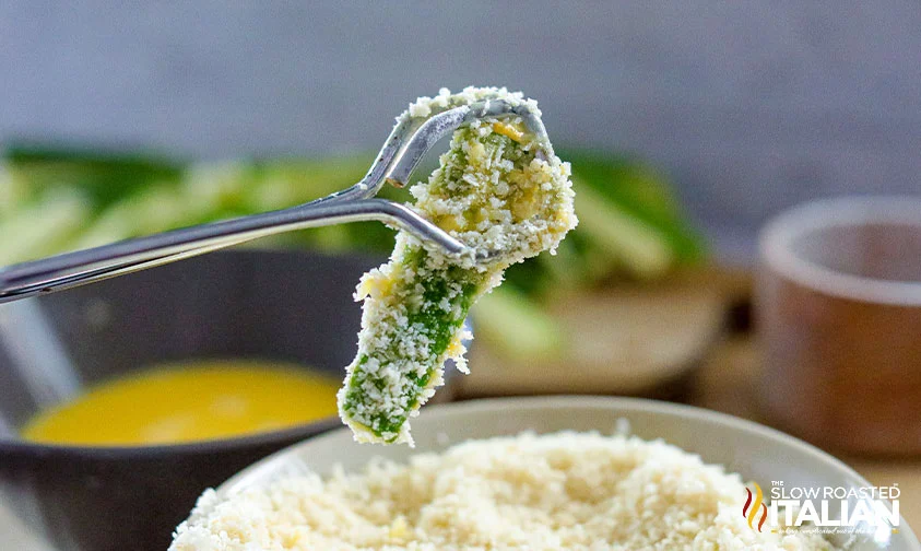 lifting coated zucchini spear out of bowl with tongs