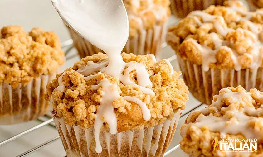 drizzling glaze over apple muffins with crumble topping