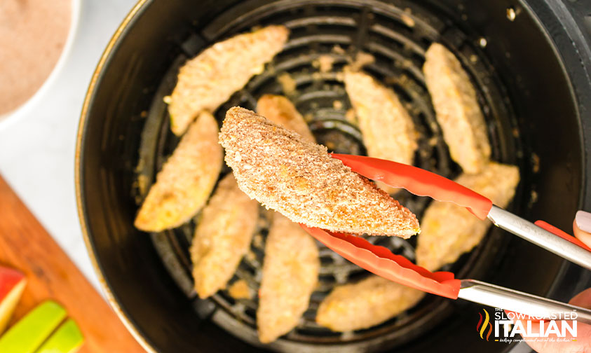 placing apple fries in air fryer with tongs