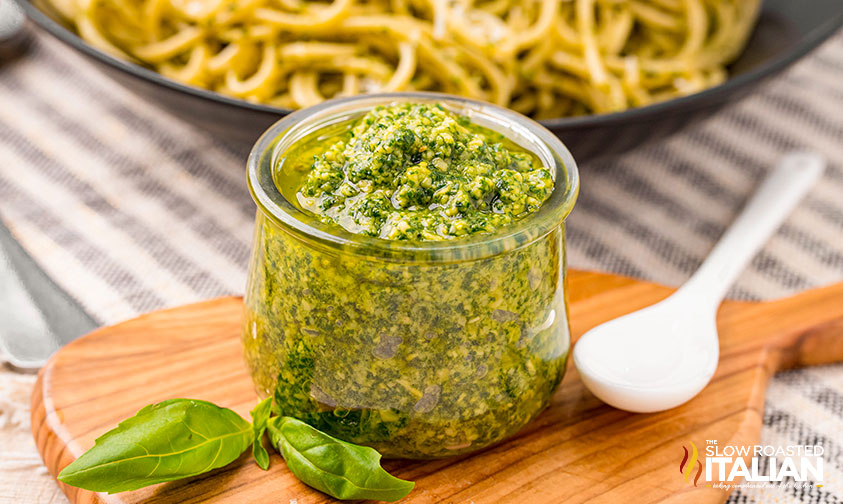 small jar of pesto with pesto spaghetti in background