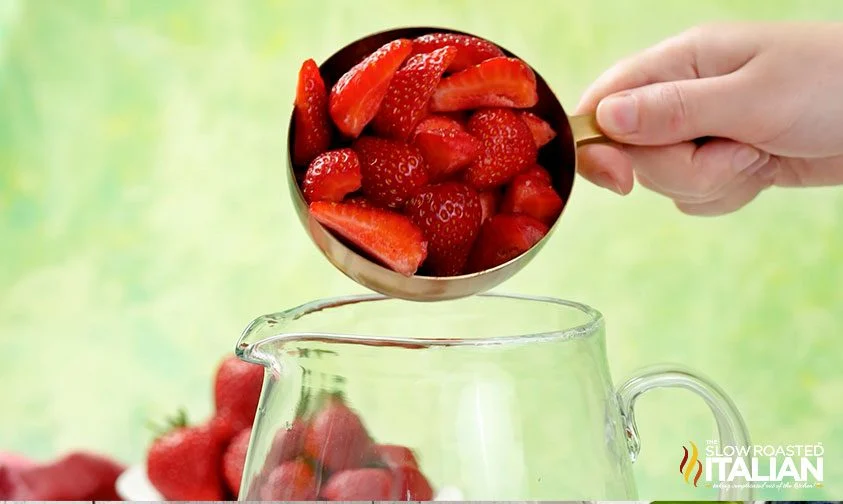 adding measuring cup of strawberries to pitcher