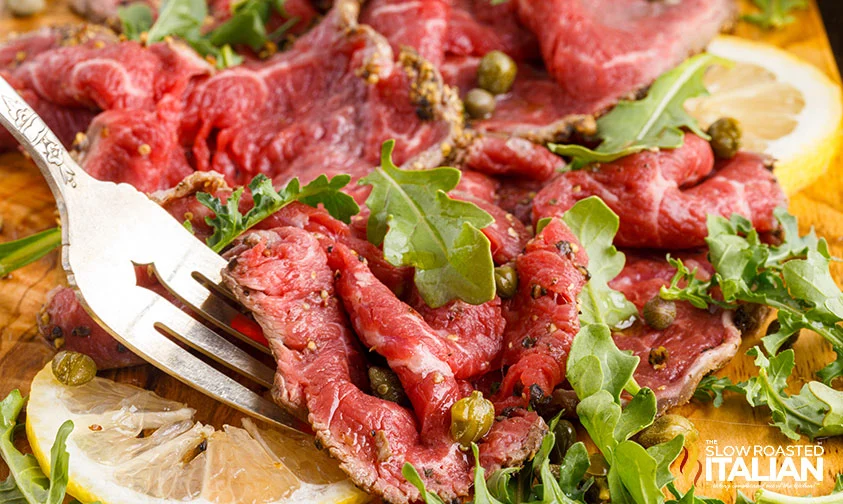 fork serving beef carpaccio with arugula