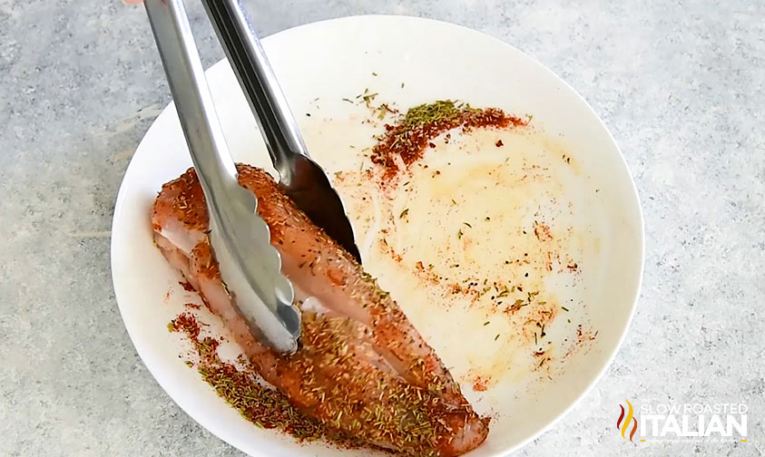 coating chicken breast in spices using tongs