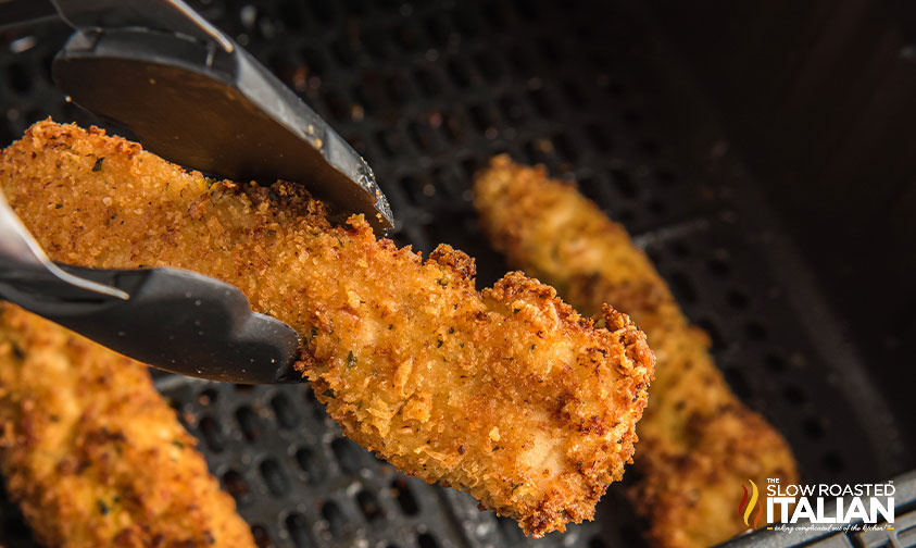 close up of tongs holding air fried chicken tender