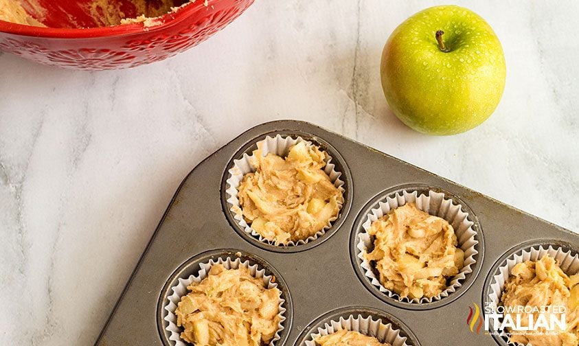 paper liners in muffin tin filled with apple muffin batter