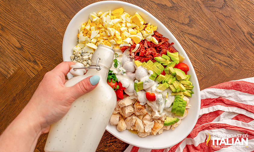 pouring creamy dressing over cobb salad ingredients