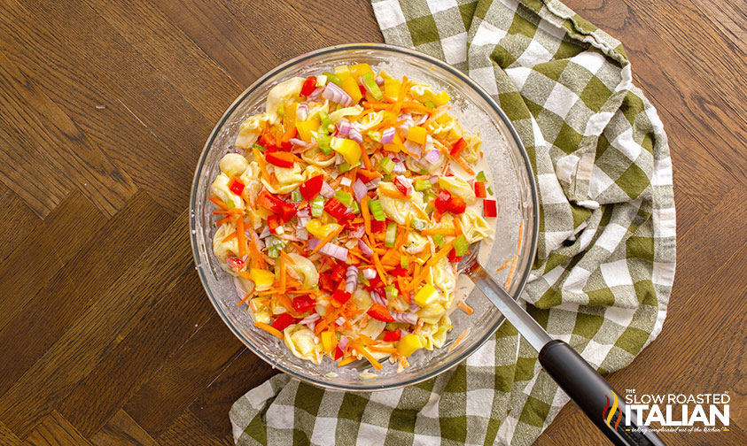 stirring together tortellini and veggies with dressing